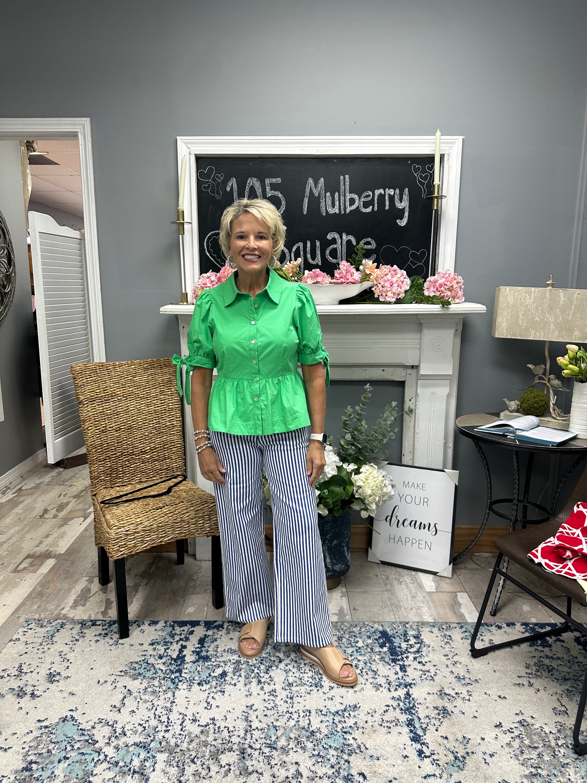 Woman in a green shirt and striped pants standing in a room with a chalkboard and decor.