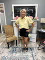 Woman in a yellow blouse and black shorts standing in a room with a fireplace and decor.