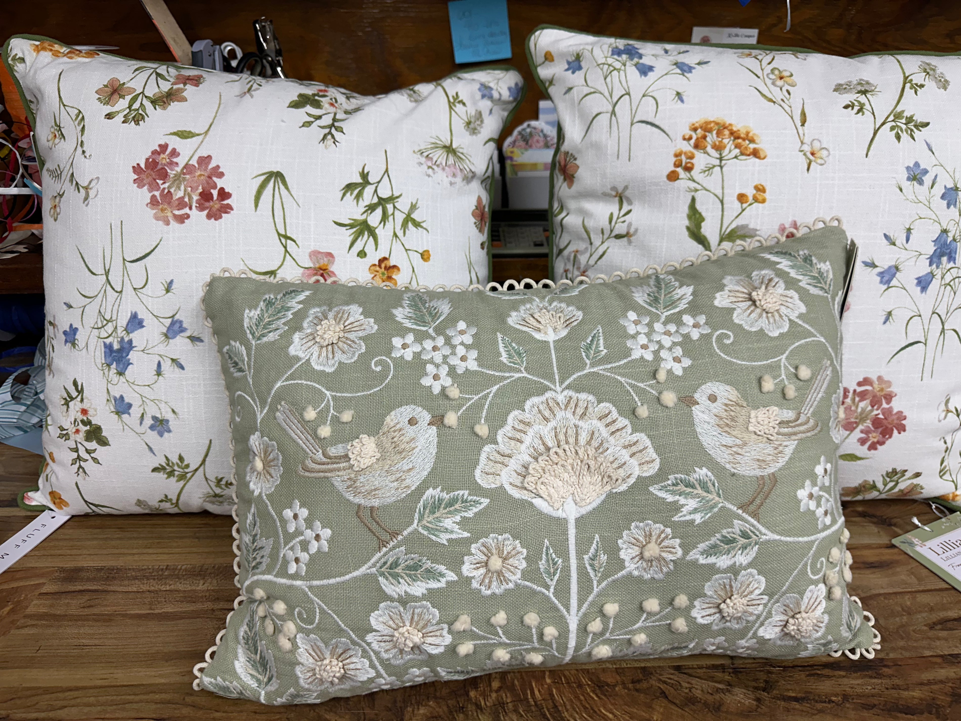 Decorative pillows with floral and bird patterns on a wooden surface.