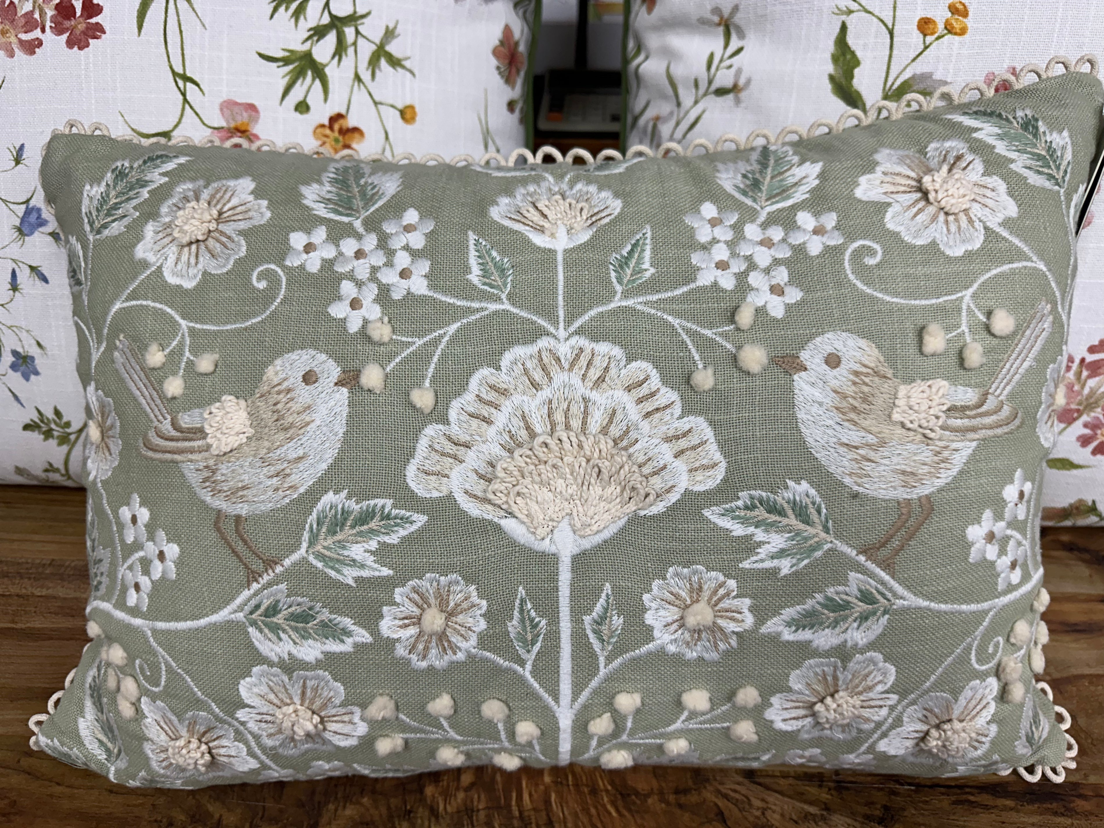 Decorative pillow with floral and bird patterns on a wooden surface.