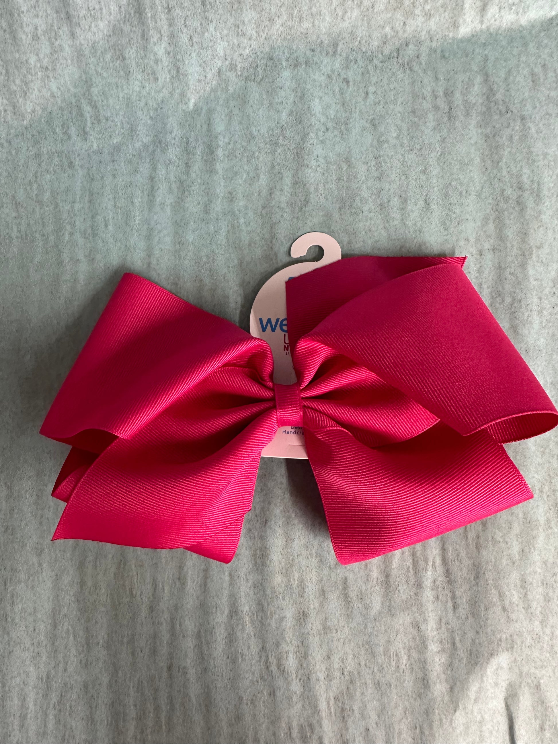 Large pink hair bow on a wooden hanger against a gray background