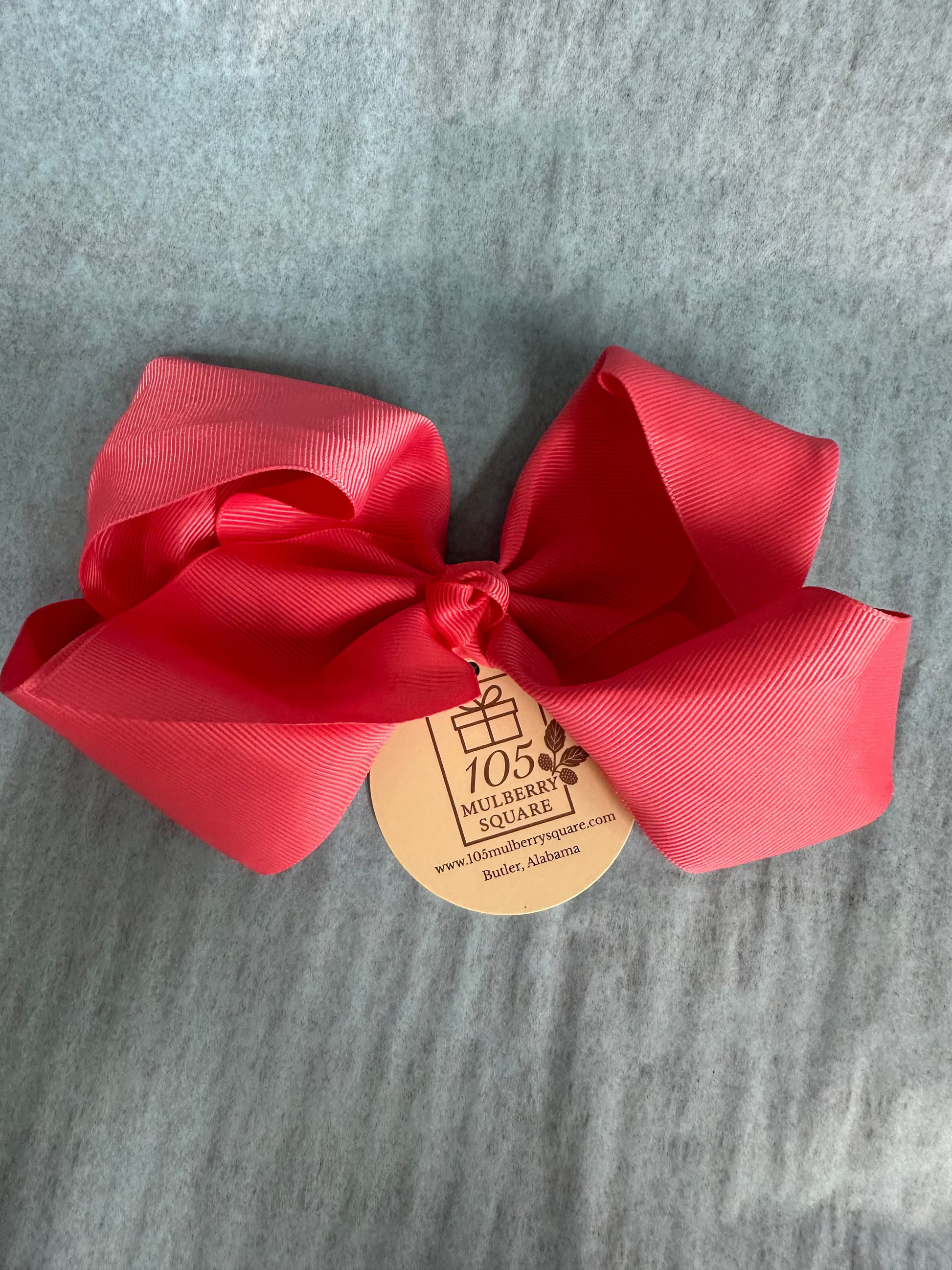 Coral bow with a brand tag on a gray background