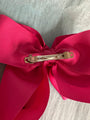 Close-up of a large pink bow with a gold clip on a textured gray background
