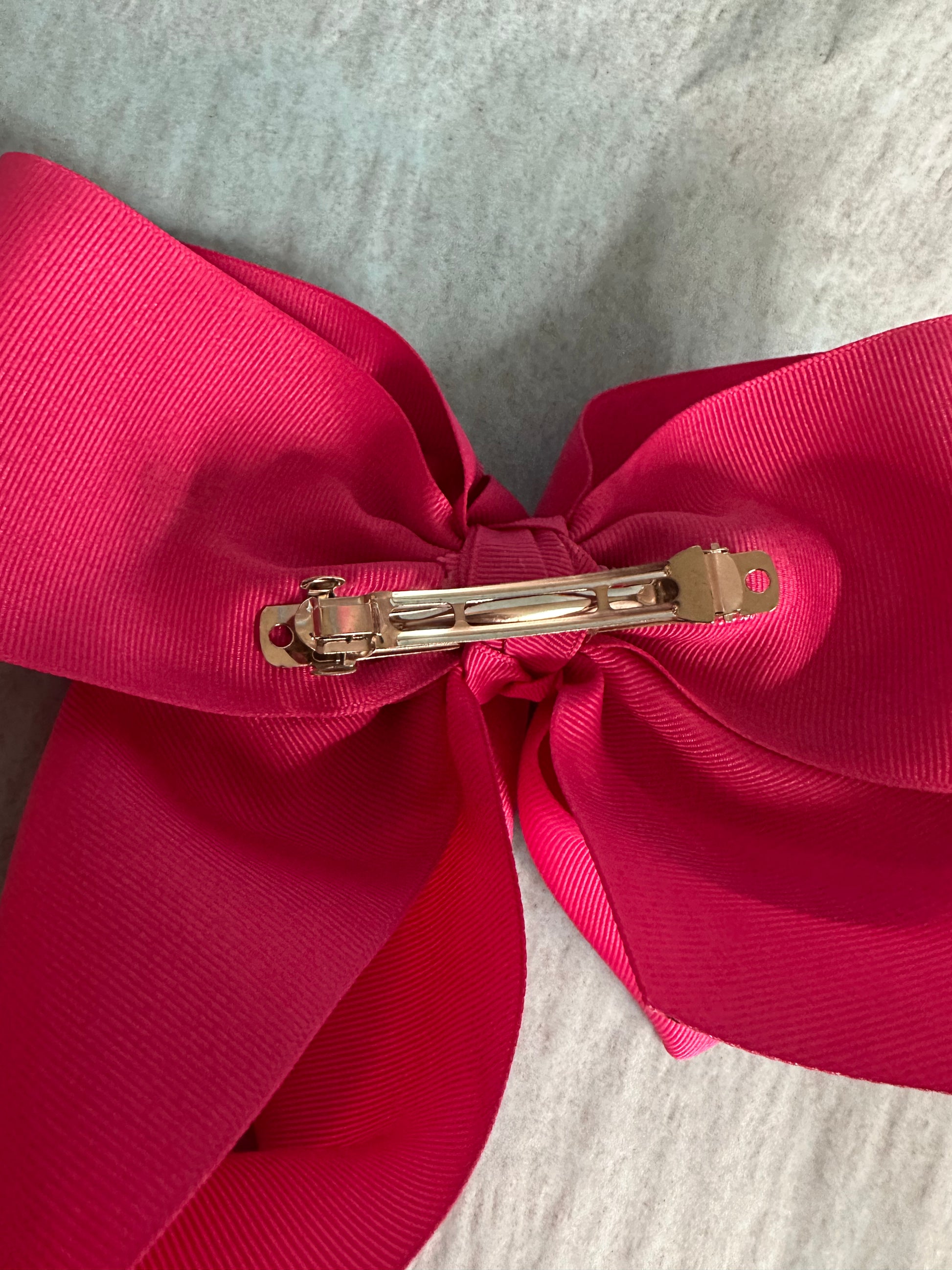 Close-up of a large pink bow with a gold clip on a textured gray background