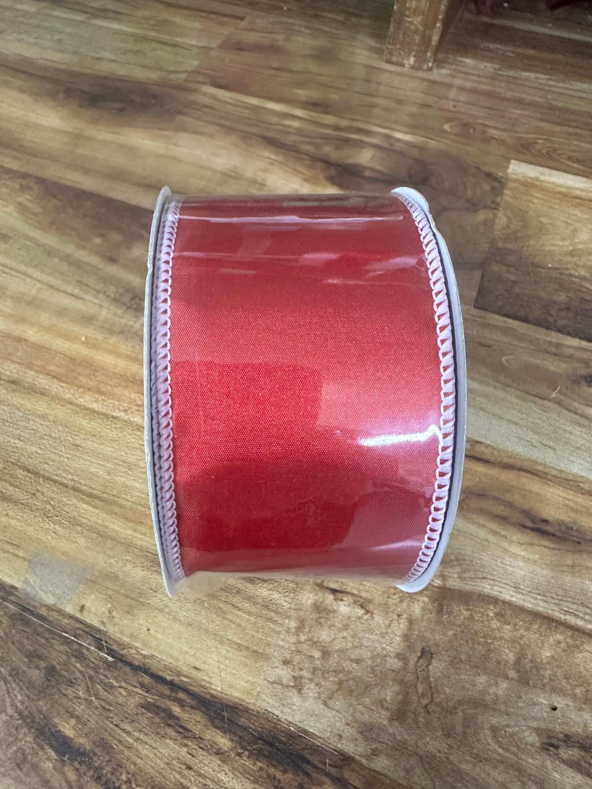 A roll of red glitter ribbon with a white serrated edge, resting on a wooden floor.