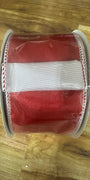 A roll of red grosgrain ribbon with a white center stripe and white stitched edges, wrapped in clear protective plastic, resting on a wooden surface.