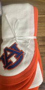 A folded white waffle-knit baby blanket with orange trim and a navy blue Auburn Tigers logo, tied with a white ribbon on a wooden surface.