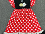 A children's dress laid flat on a gray textured surface, featuring a red and white polka-dot skirt, a black bodice, and matching red and white polka-dot ruffled shoulder straps.