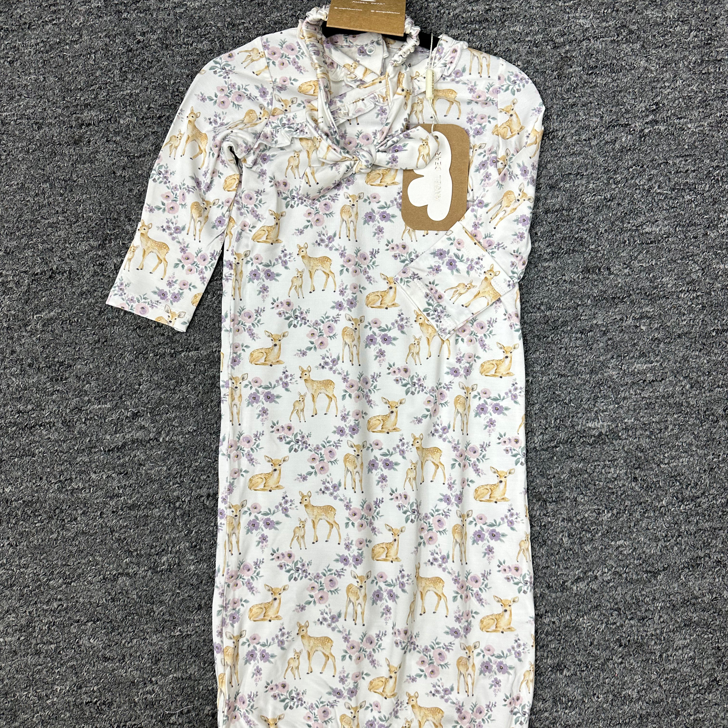 A baby sleep sack with a white background, featuring a repeating pattern of yellow deer and purple flowers, hanging on a black hanger against a dark gray textured carpet.