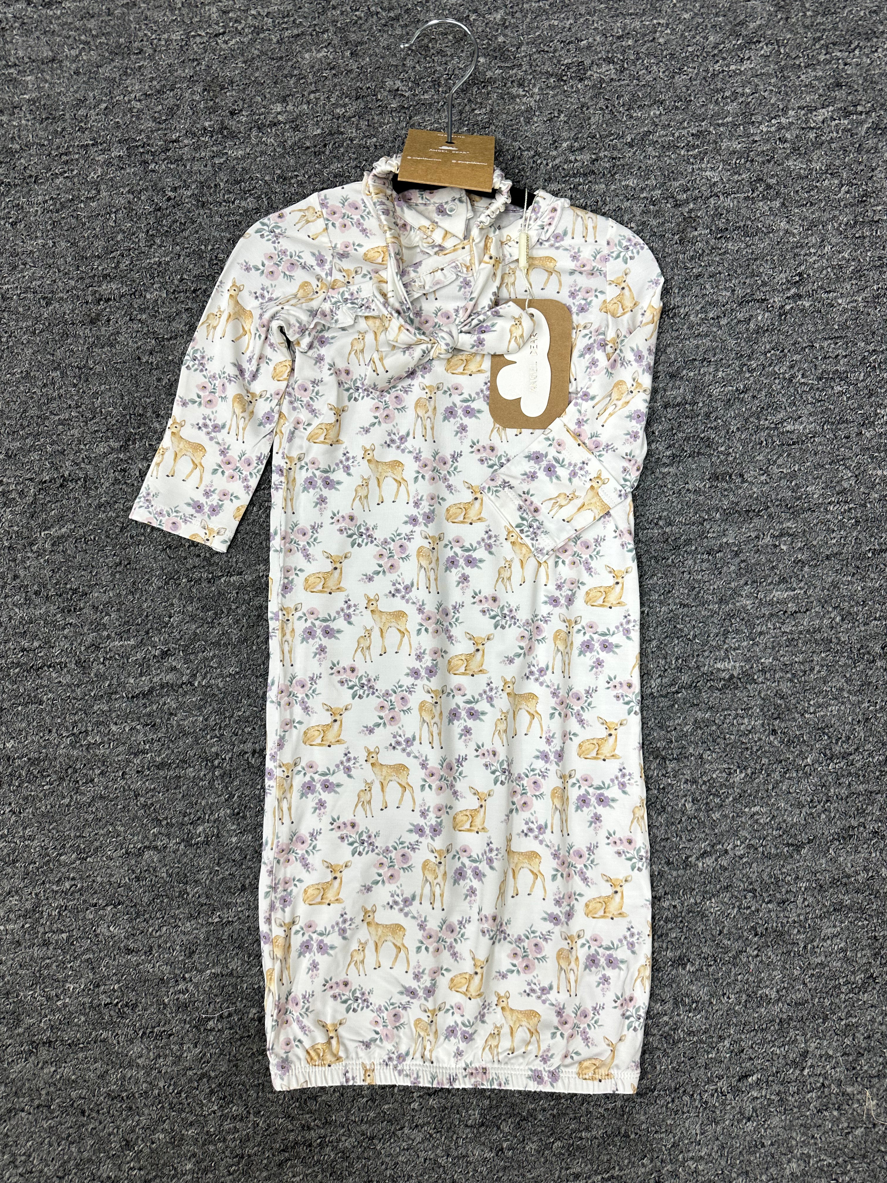 A baby sleep sack with a white background, featuring a repeating pattern of yellow deer and purple flowers, hanging on a black hanger against a dark gray textured carpet.