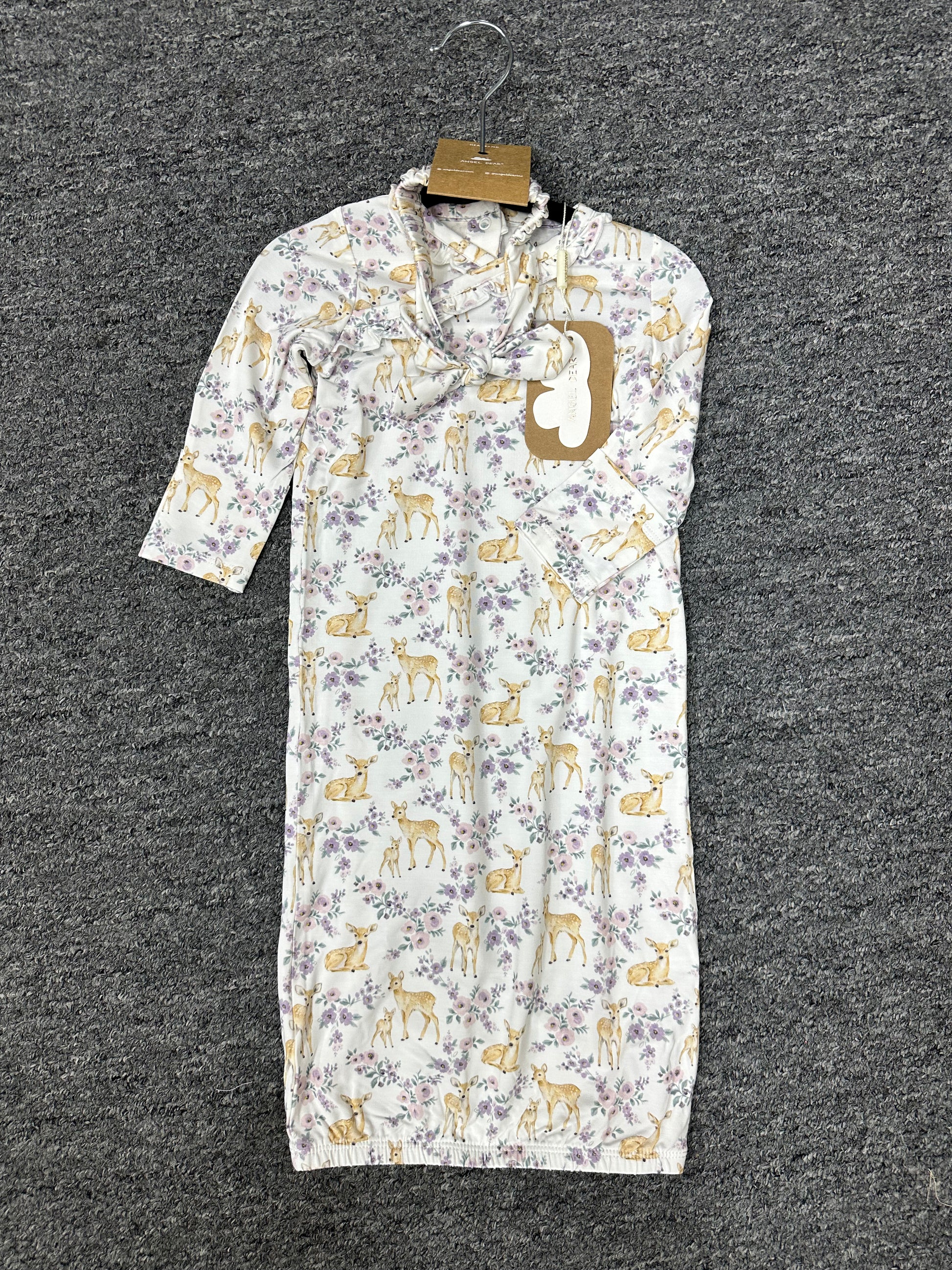 A baby sleep sack with a white background, featuring a repeating pattern of yellow deer and purple flowers, hanging on a black hanger against a dark gray textured carpet.