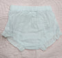 A pair of light mint green baby bloomers with eyelet lace trim, laid flat on a pink quilted blanket.