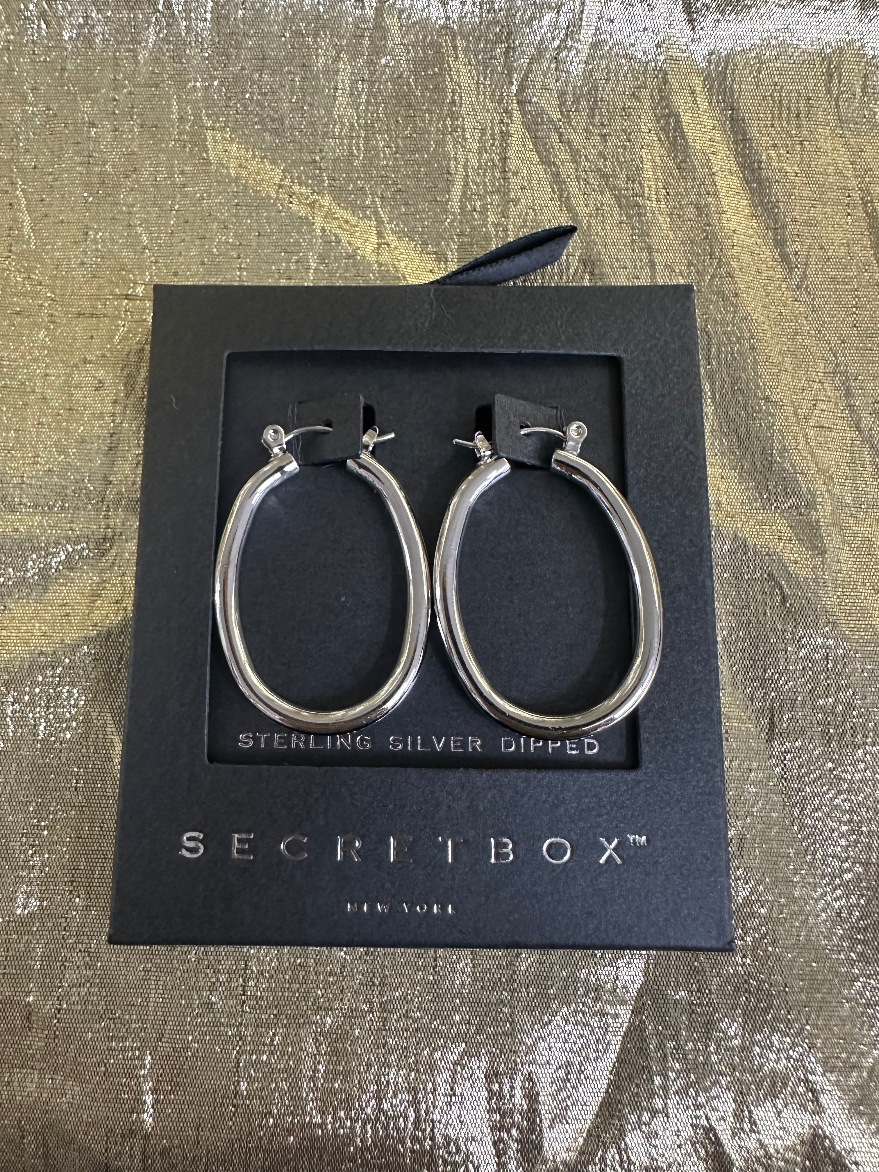 Sterling silver hoop earrings displayed on a black Secretbox gift box, set against a textured gold and brown background.