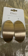 A pair of large oval drop earrings with a brushed gold finish, attached to a white display card labeled 'Cloie Jewelry & Crafts' and placed on a textured gold surface.