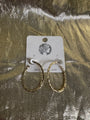 A pair of textured gold hoop earrings displayed on a white cardboard backing card, set against a shiny, crinkled metallic gold background.