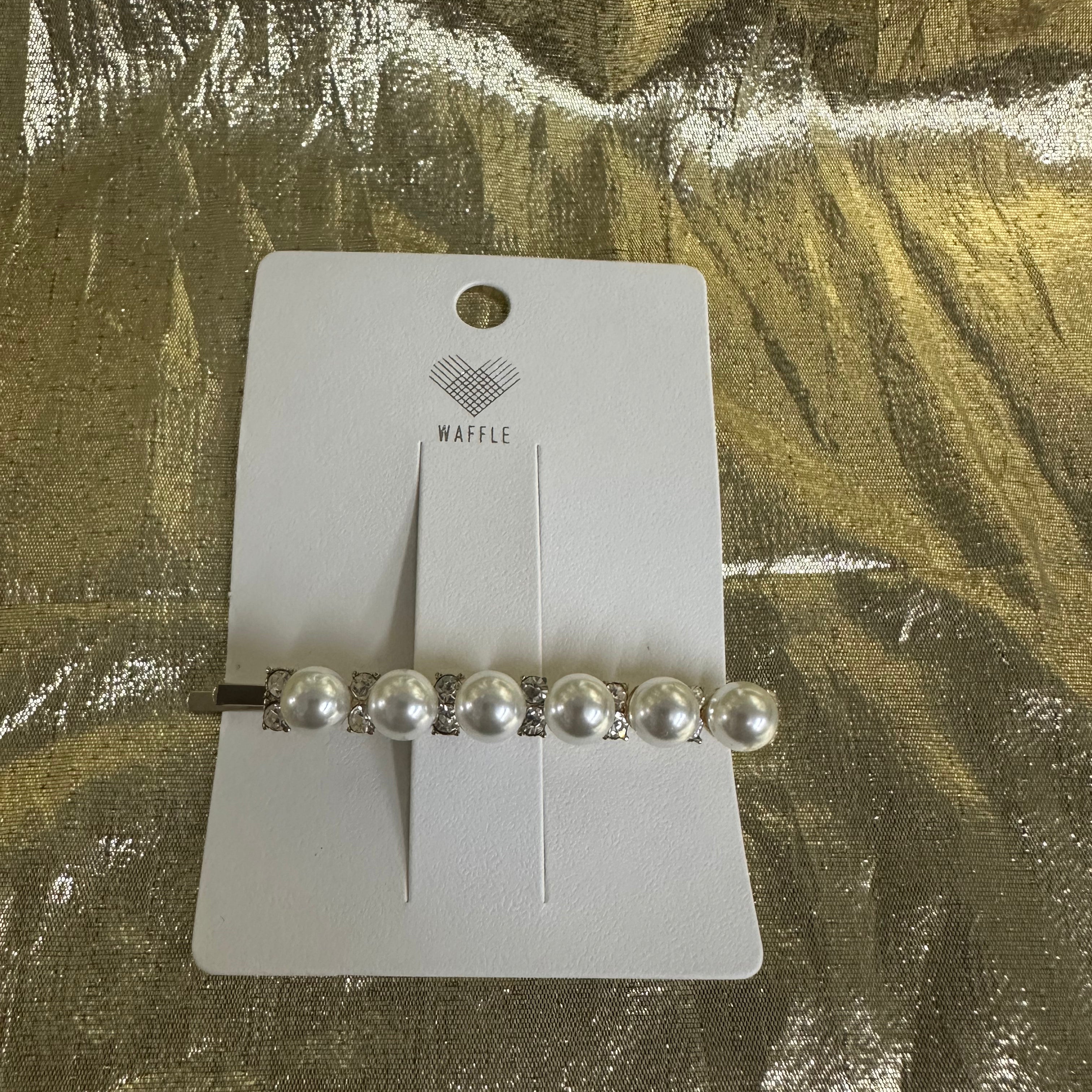 A silver barrette hair clip with five white faux pearls and rhinestone accents, displayed on a white Waffle brand card over a textured gold foil background.