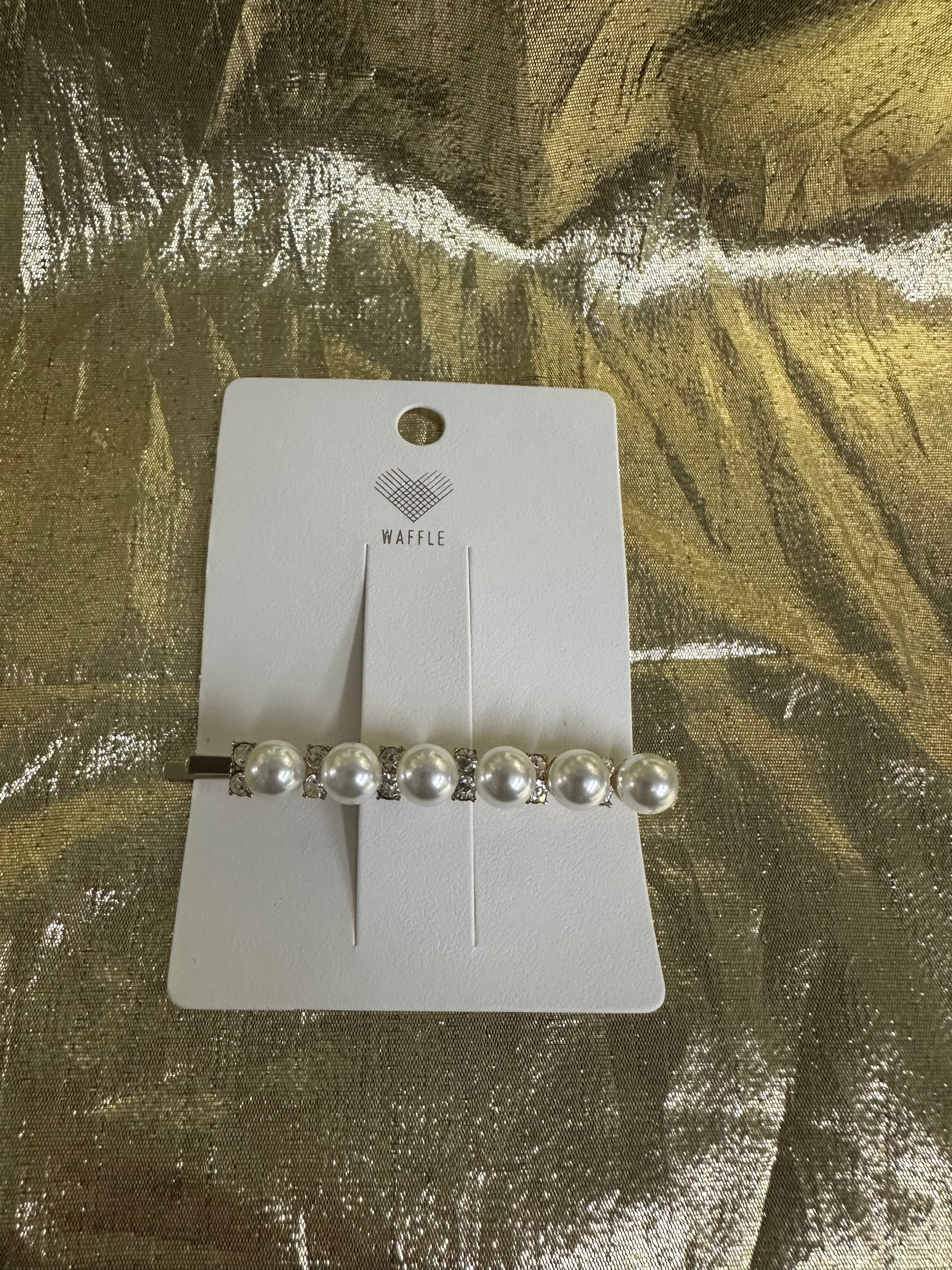 A silver barrette hair clip with five white faux pearls and rhinestone accents, displayed on a white Waffle brand card over a textured gold foil background.