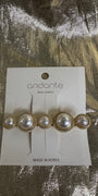 Andante gold and pearl hair clip on a white display card, photographed on a textured gold foil background.