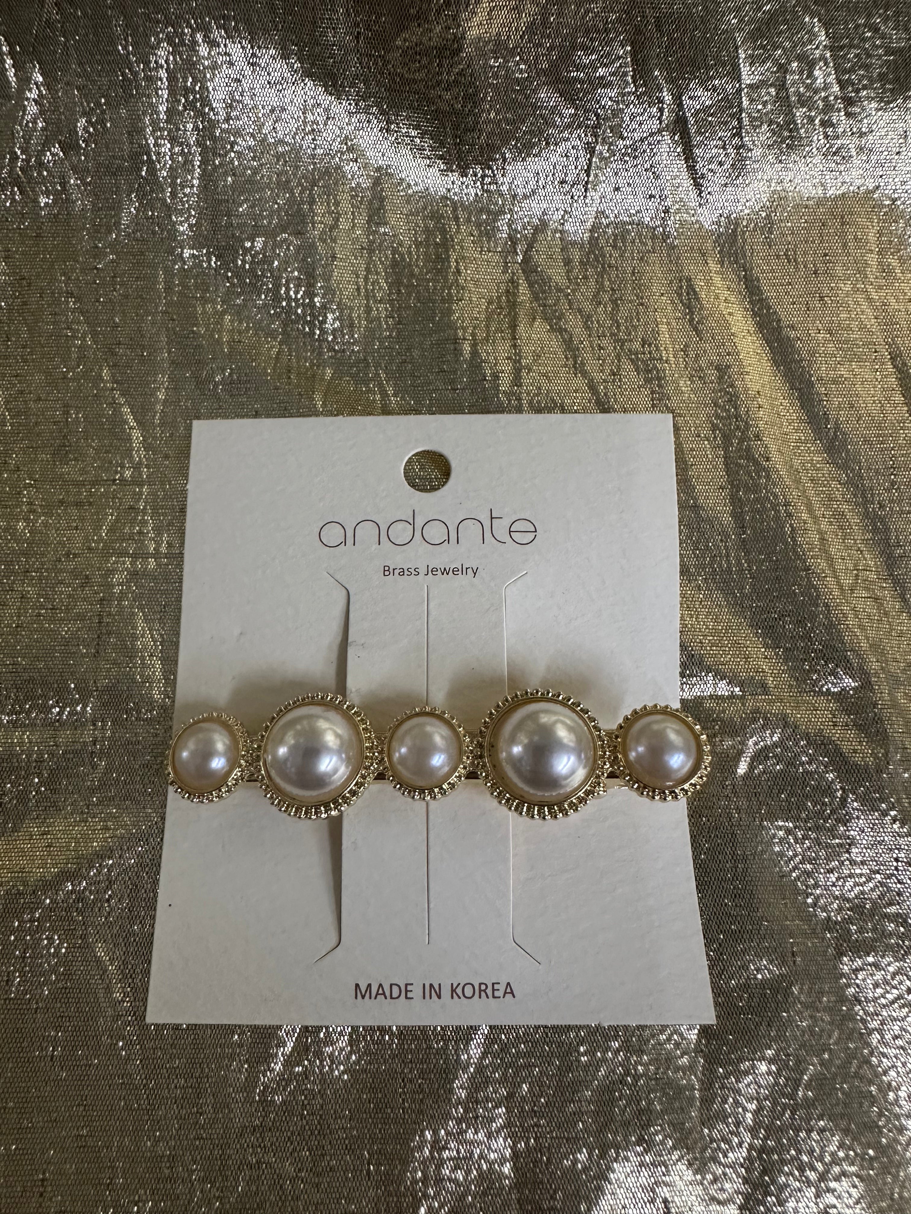 Andante gold and pearl hair clip on a white display card, photographed on a textured gold foil background.