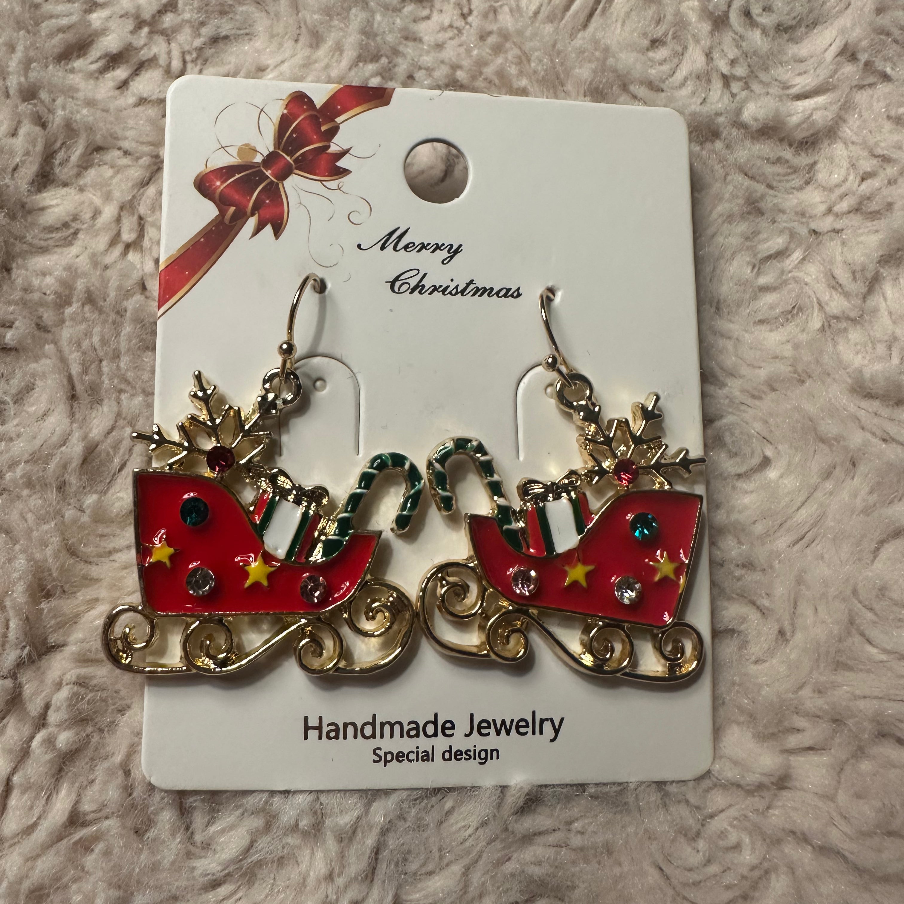 Sleighs earrings filled with gifts on white card with "Merry Christmas" in cursive and red and gold bow