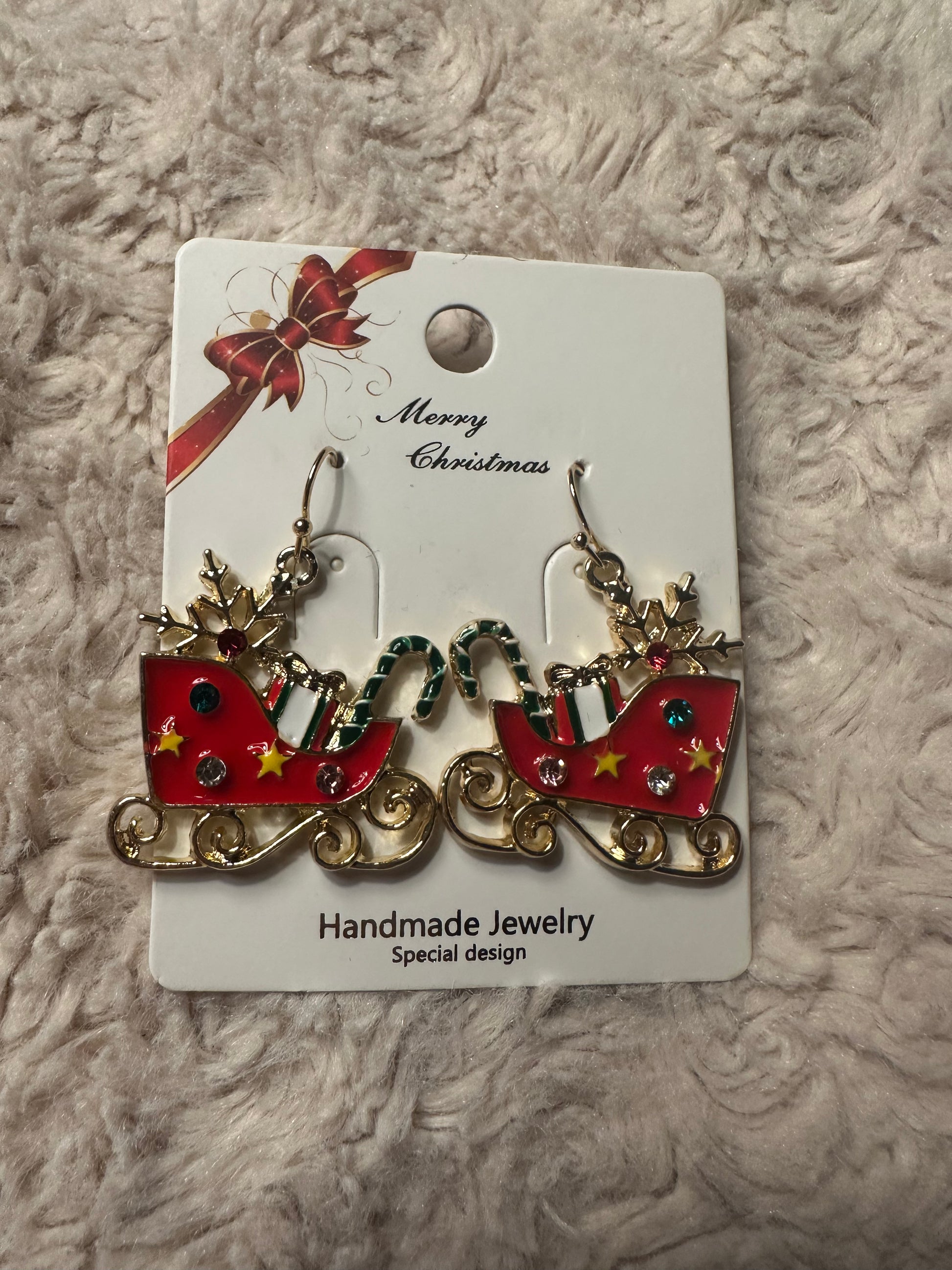 Sleighs earrings filled with gifts on white card with "Merry Christmas" in cursive and red and gold bow