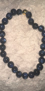 A beaded necklace made of dark blue, semi-translucent round beads with a small gold accent bead near the clasp, displayed on a textured white fabric background.