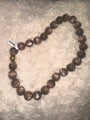 A strand of large, polished brown glass beads with a small gold-toned accent bead, laid out on a textured white faux fur surface.