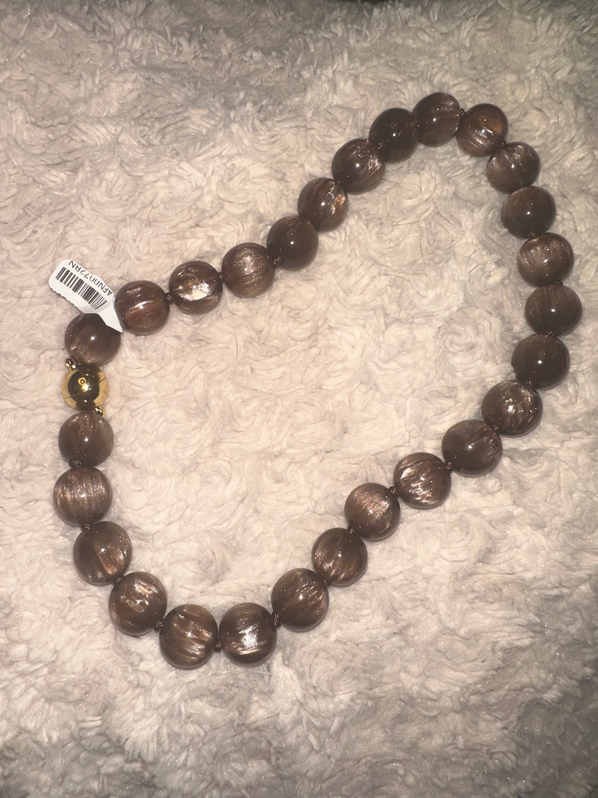 A strand of large, polished brown glass beads with a small gold-toned accent bead, laid out on a textured white faux fur surface.