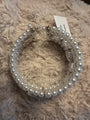 A white faux-pearl cuff bracelets with silver-toned metal clasps and a small paper tag, displayed on a beige shaggy blanket.