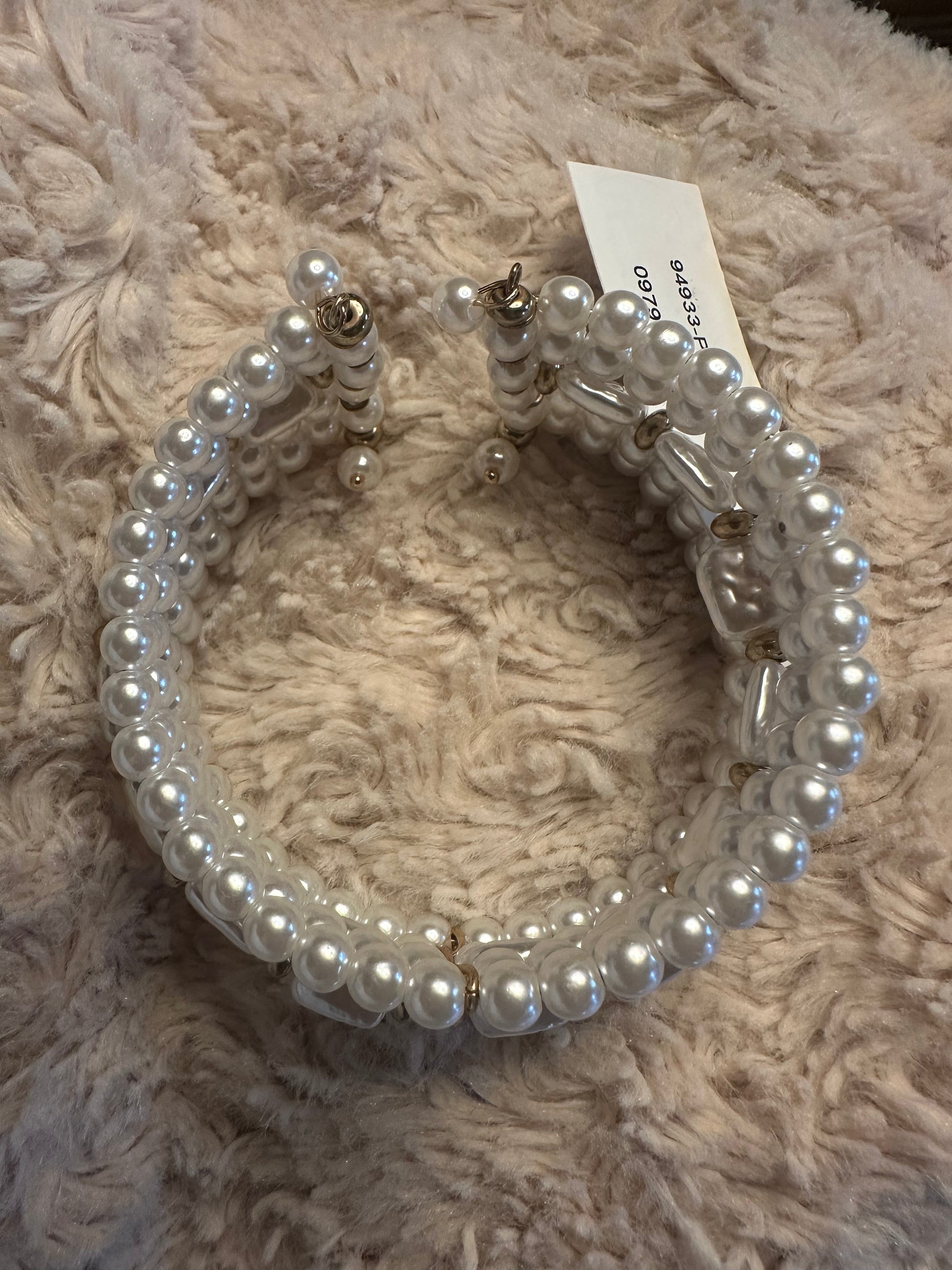 A white faux-pearl cuff bracelets with silver-toned metal clasps and a small paper tag, displayed on a beige shaggy blanket.