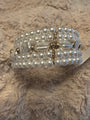 A multi-strand pearl beaded bracelet with gold-toned metal accents and a central clear faceted bead, resting on a textured beige faux fur surface.