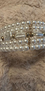 A multi-strand pearl beaded bracelet with gold-toned metal accents and a central clear faceted bead, resting on a textured beige faux fur surface.