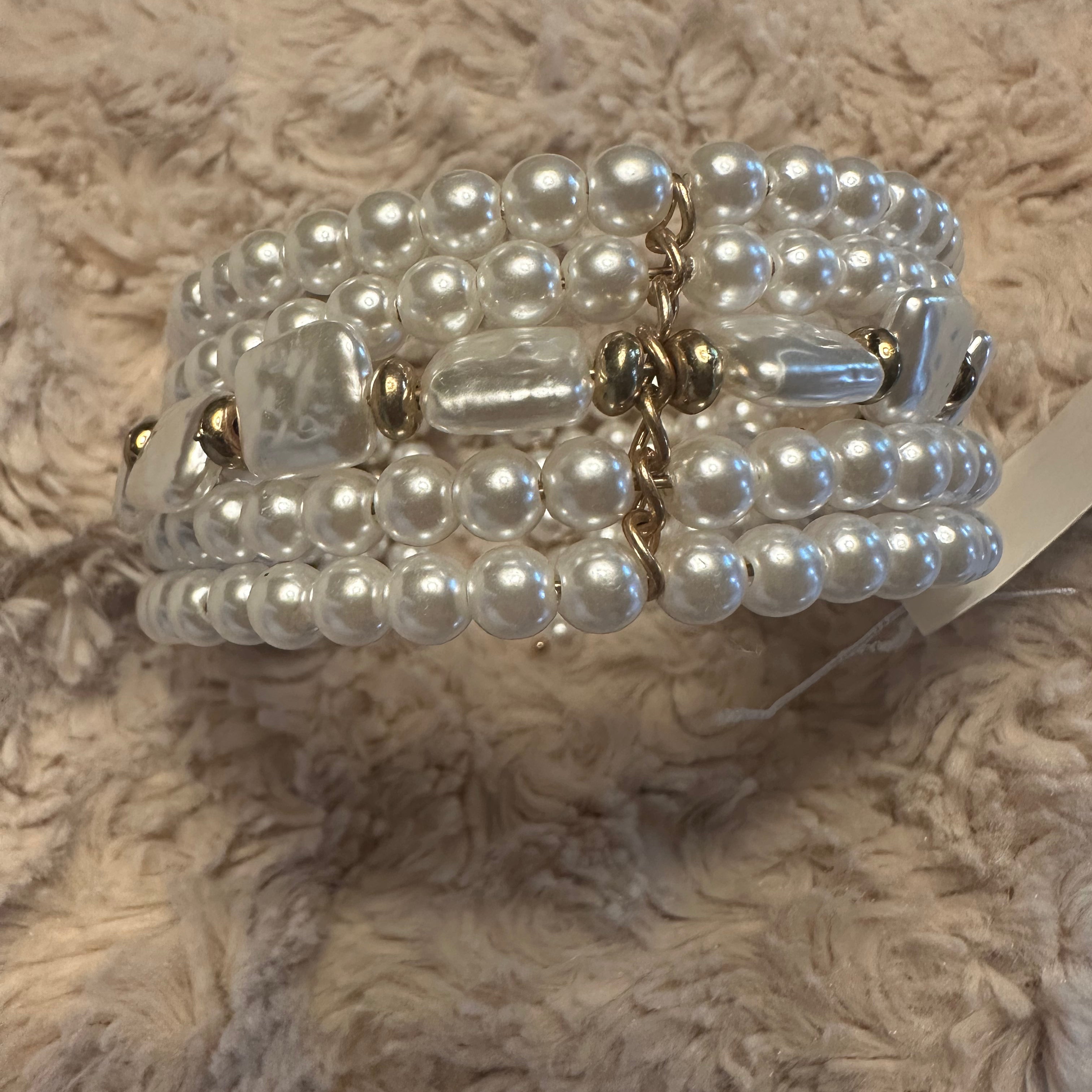 A multi-strand pearl beaded bracelet with gold-toned metal accents and a central clear faceted bead, resting on a textured beige faux fur surface.