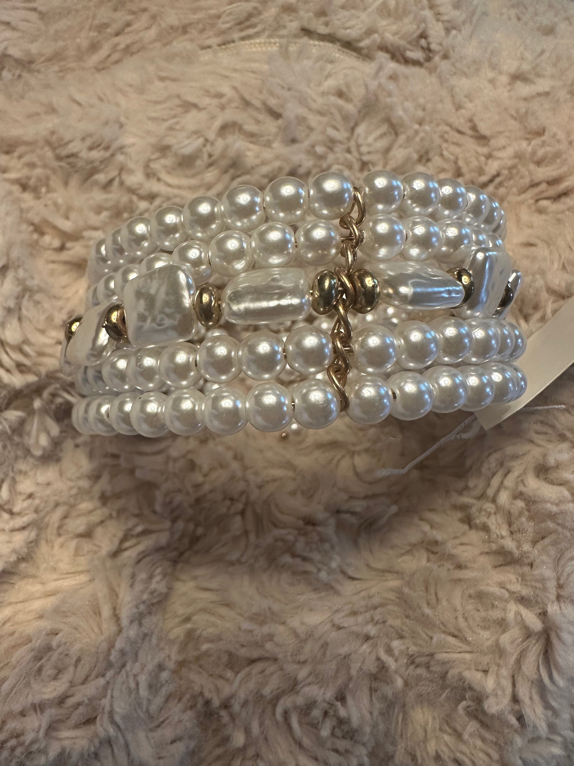 A multi-strand pearl beaded bracelet with gold-toned metal accents and a central clear faceted bead, resting on a textured beige faux fur surface.