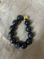 A beaded bracelet made of glossy black round beads with a small gold-toned clasp, photographed on a wrinkled beige fabric background.