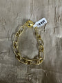 A gold-toned chunky chain link bracelet with a spherical clasp and a white barcode tag, displayed on a textured metallic gold fabric background.