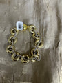 A gold and silver-tone chain link bracelet with large interlocking rings, shown on a textured metallic gold fabric background with a white barcode tag attached.