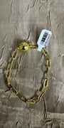 A gold chain bracelet with a polished ball clasp, laid flat on a textured beige fabric background with a white product tag attached.