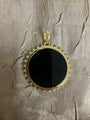 A round black pendant with a gold-tone beaded border and top loop, displayed on a textured beige fabric background.