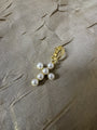A gold-toned clip-on earring featuring four white faux pearls arranged in a curved line, resting on a textured beige fabric background.
