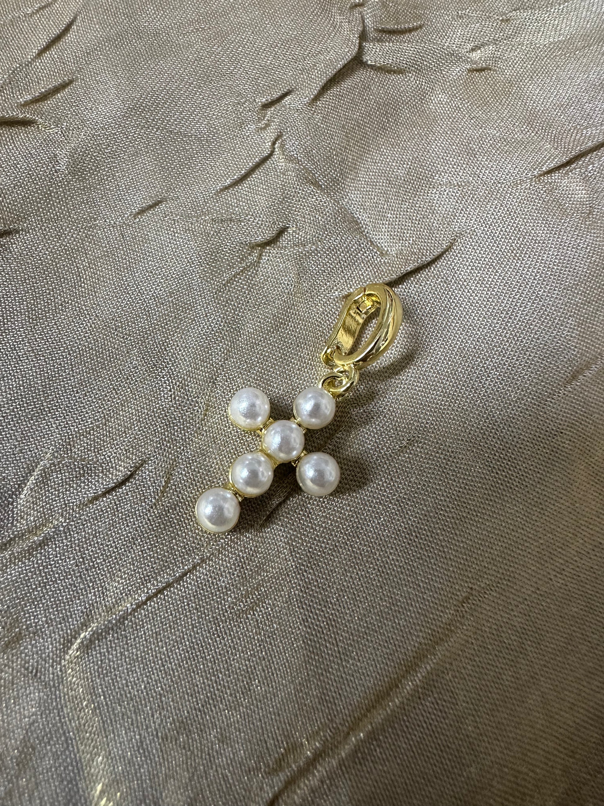 A gold-toned clip-on earring featuring four white faux pearls arranged in a curved line, resting on a textured beige fabric background.
