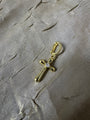 A gold cross charm with a small clear gemstone at the center, attached to a gold lobster clasp, displayed on a textured gray fabric background.