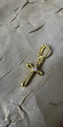 A gold cross charm with a small clear gemstone at the center, attached to a gold lobster clasp, displayed on a textured gray fabric background.