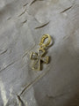 A gold cross pendant charm embellished with clear crystals, resting on a textured silver fabric background.