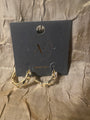 Gold hoop earrings with clear crystal-like accents, displayed on a black branded jewelry card against a textured beige fabric background.