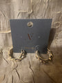 A pair of chunky gold hoop earrings with textured, organic edges, displayed on a dark gray branded card against a crinkled gold fabric background.