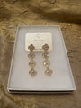 A pair of gold-toned dangle earrings with clear rhinestones, presented on a white jewelry card inside a white box, set against a textured gold fabric background. The brand name 'FULIJA' is visible on the card.