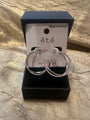 A pair of large silver hoop earrings with clear rhinestone-like stones, displayed in an open black jewelry box with a white card labeled “été” and “Water-Resistant.”.