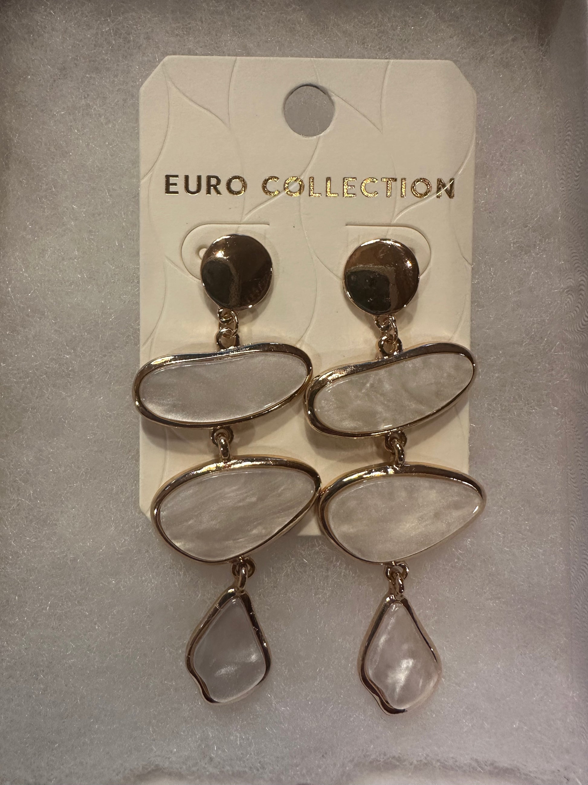 A pair of gold-tone drop earrings with three stacked irregular oval stone-like charms and a teardrop dangling charm, attached to a white display card labeled EURO COLLECTION.