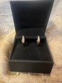 A pair of gold hoop earrings with pavé-set clear stones, displayed inside an open black jewelry box on a textured gold fabric background.